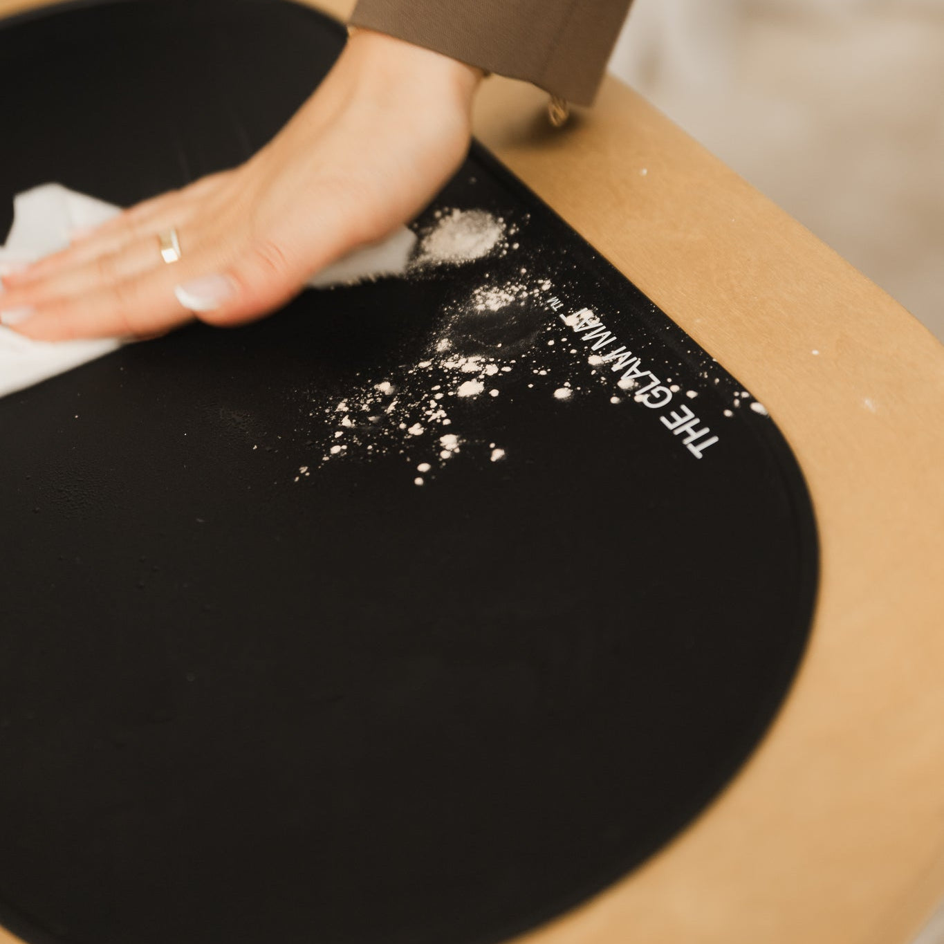 Person cleaning a black mat with white powder, branded 'THE GLAM MAT'