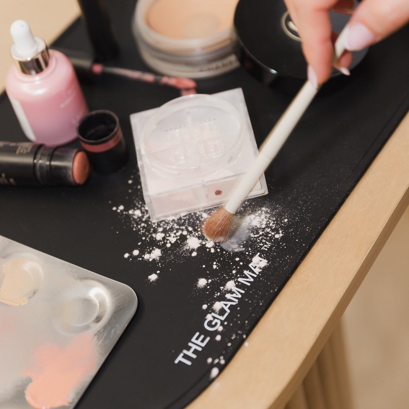Makeup application on a black mat with 'The Glam Man' branding, featuring various makeup items.
