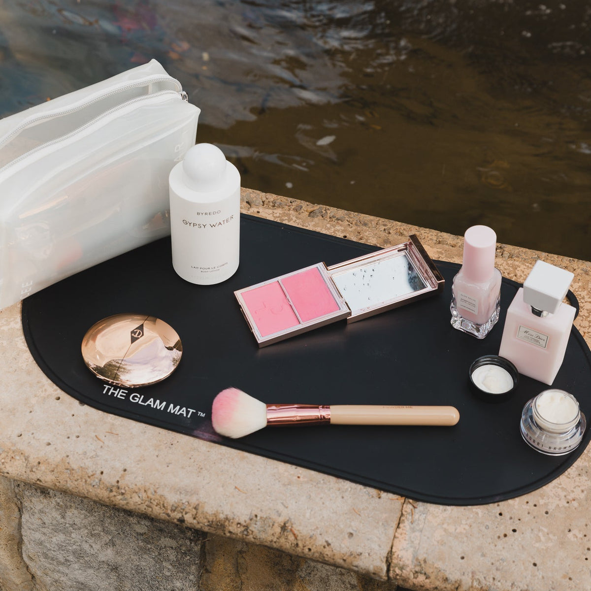Makeup products on a black mat by a body of water